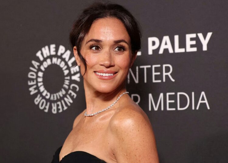 Meghan Markle posing elegantly on the red carpet in a designer gown, smiling for photographers.