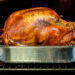 A roasted turkey in a metal pan inside an oven, golden brown and seasoned.