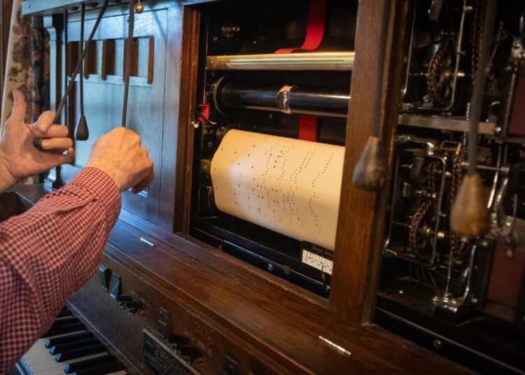 A man's hand pulls levers near a roll of music in a photoplayer.
