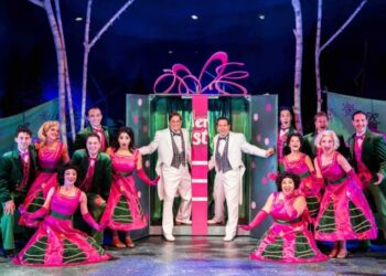 Cast members pose around a large gift box on stage.
