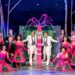 Cast members pose around a large gift box on stage.