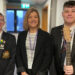 Music teacher Sharon Baird, wearing a black blazer over a white top with black stripes, stands between pupils Matthew McGibbon and Deacon Weary. Both teenage boys are dressed in shirt, tie and blazer, which has the school crest embroidered on the breast. Matthew is tall with dark hair and holds a guitar in his left hand. Deacon is shorter, with fair hair and glasses.