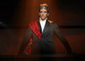 Michael Urie standing in a suit with a crown on his head