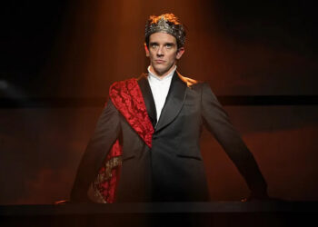 Michael Urie standing in a suit with a crown on his head