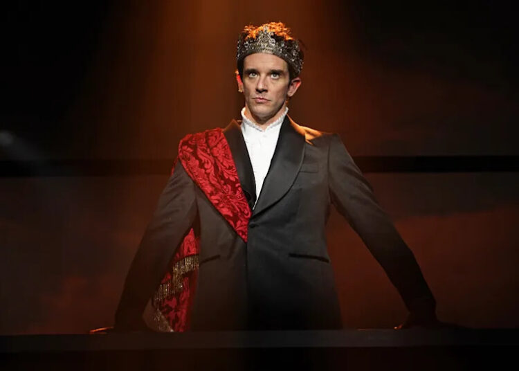 Michael Urie standing in a suit with a crown on his head