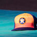 An orange and blue ball cap with the Houston Astros logo on it while it rests on a blue table.