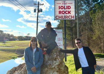 Image of three men posing for the camera by a green field