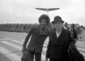 Jimi Hendrix poses with a fellow passenger on the runway as he arrives at Hamburg airport on Sept. 5, 1970. (AP Photo/Helmuth Lohmann)