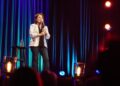 Kathleen Madigan standing on stage holding a mic