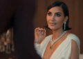 A person in elegant evening attire with a deep neckline and statement jewelry, seated at a formal event