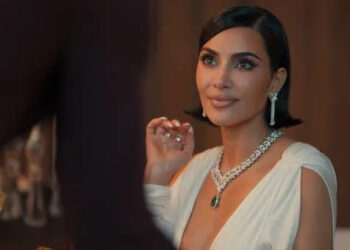 A person in elegant evening attire with a deep neckline and statement jewelry, seated at a formal event