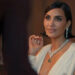 A person in elegant evening attire with a deep neckline and statement jewelry, seated at a formal event