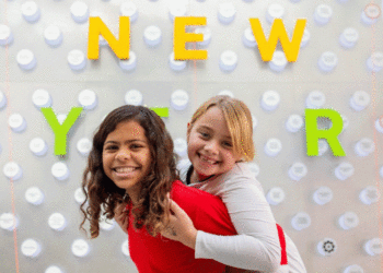 Two kids play piggy-back in front of a Happy New Year sign. (Courtesy photo)
