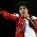 Michael Jackson performing energetically on stage, wearing a red sequined jacket and holding a microphone.