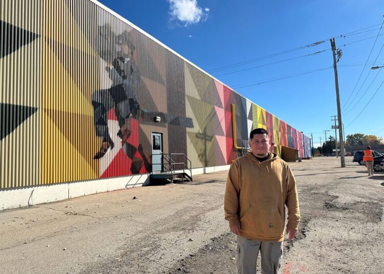Photo of Mauricio Martinez with his mural in Oshkosh.
