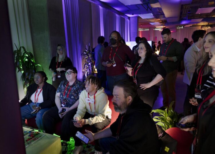 People wearing lanyards sit around a screen.