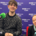 A 20-year-old man and 13-year-old girl sit in front of microphones in a radio studio, smiling at the camera.