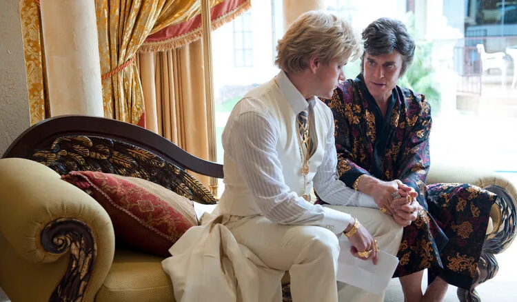 Matt Damon as Scott sitting on the sofa and holding hands with Michael Douglas as Liberace in Behind the Candelabra