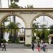 People pass by the main gate to Paramount Studios on Melrose Avenue, Wednesday, July 8, 2015, in Los Angeles. Paramount Pictures chiseled a crack into the closely guarded theatrical window on Wednesday, July 8, 2015, in an experimental agreement with two leading theater chains that will trim the length of time a handful of movies are restricted to playing only in theaters. Paramount, along with AMC Theaters and Cineplex Entertainment, announced a deal to shorten the rollout of two low-budget horror films due out in October: Paramount's "Paranormal Activity: The Ghost Dimension" and "Scout's Guide to the Zombie Apocalypse." (AP Photo/Nick Ut)