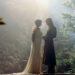 Two characters in flowing robes stand facing each other in a mystical forest setting, surrounded by lush greenery and soft, ethereal light