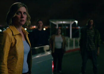Rhea Seehorn as Carol Sturka looking worriedly at several people surrounding her in Pluribus