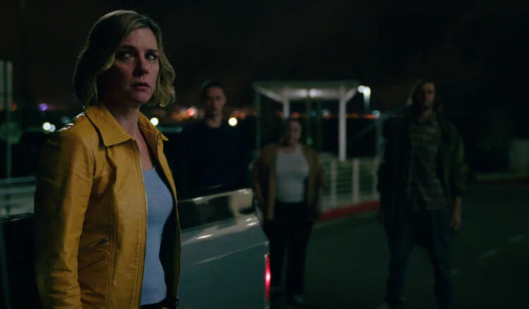 Rhea Seehorn as Carol Sturka looking worriedly at several people surrounding her in Pluribus