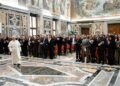 Pope Leo walks across a marbled floor in front of a large group of people assembled in rows.