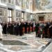 Pope Leo walks across a marbled floor in front of a large group of people assembled in rows.