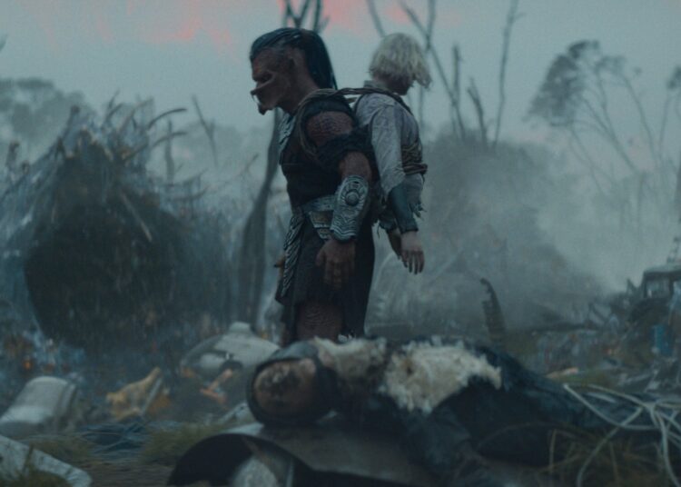 A Yautja alien with a humanoid robot missing her legs strapped to its back.