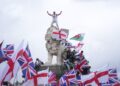 A demonstrator stands on the head of the South Bank lion that sits on the side of the Westminster Bridge, during a Tommy Robinson-led Unite the Kingdom march and rally in London, Saturday, Sept. 13, 2025. (AP Photo/Joanna Chan)