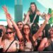 A crowd of people in a big festival tent with hands up and smiling into the camera. Someone is up on their friends shoulders and one girl is holding a "defected records" fan.