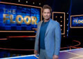 Rob Lowe standing on The Floor in a blue suit and tee and looking right at the camera before a taping.
