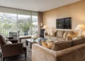 Spacious living room of Ozzy and Sharon Osbourne’s West Hollywood condo, featuring marble floors, recessed lighting, a grand piano, and floor-to-ceiling glass walls with Hollywood Hills views.