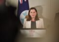 Deb Frecklington stands in white blazer in front of parliamentary flag with Queensland Government logo