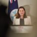 Deb Frecklington stands in white blazer in front of parliamentary flag with Queensland Government logo