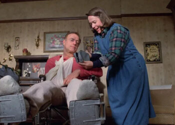 Paul sitting in a wheelchair next to Annie in Misery
