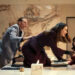 A lively boardroom scene with four people, including one standing on a table. They're engaged in an animated discussion