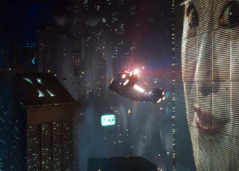 Wide shot of Los Angeles skyline in Blade Runner, including a car flying through air and woman on giant billboard