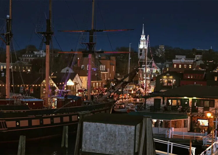 A shot of the city of Newport lit up at night with a sail boat in the foreground in A Newport Christmas.
