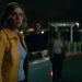 Rhea Seehorn's Carol Sturka standing beside a car with ominous figures on the background on Pluribus