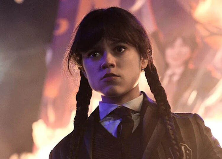 Jenna Ortega's Wednesday standing in front of a burning picture of herself in Wednesday Season 2.