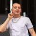 Aitch, in a white t-shirt, puts his finger to his ear on stage at TRNSMT.