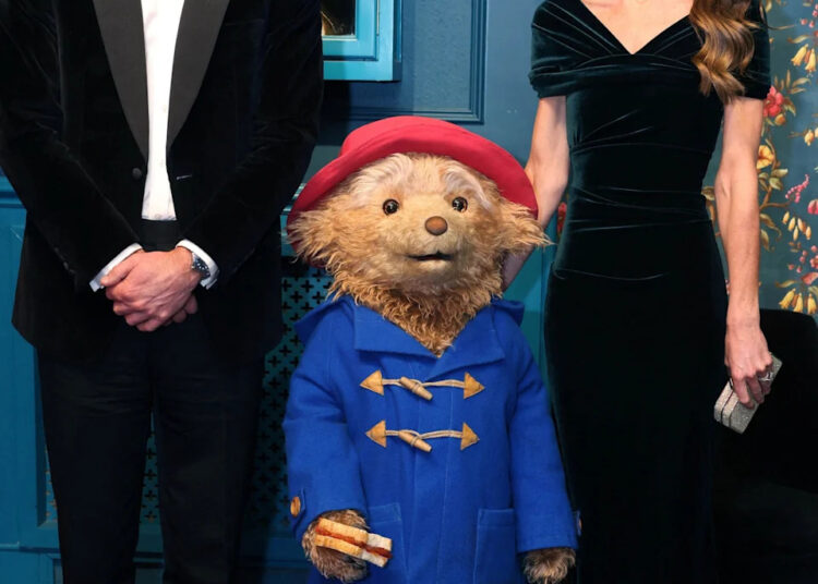 The Prince and Princess of Wales posing either side of Paddington - Catherine has her hand on the back of the bear's head