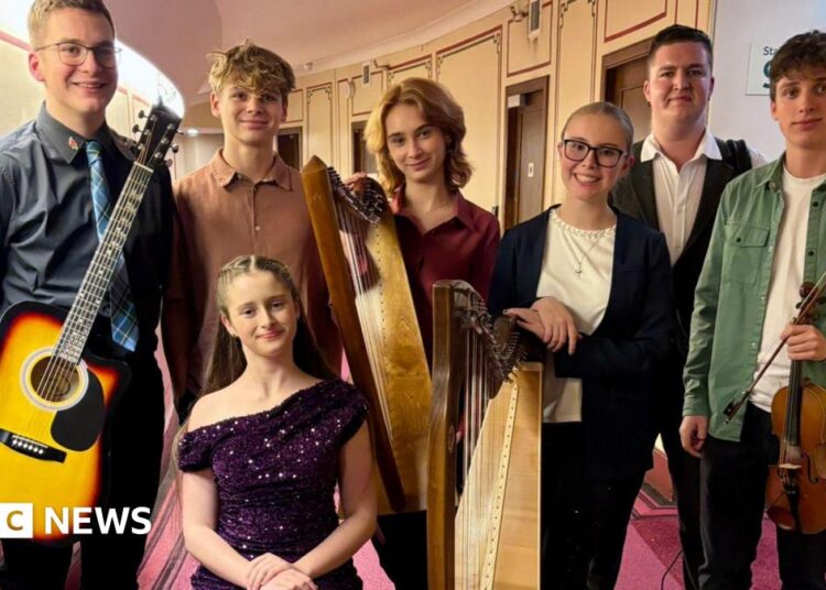 Seven members of Scran stand in a group holding their musical instruments. They are aged between 13 and 17.