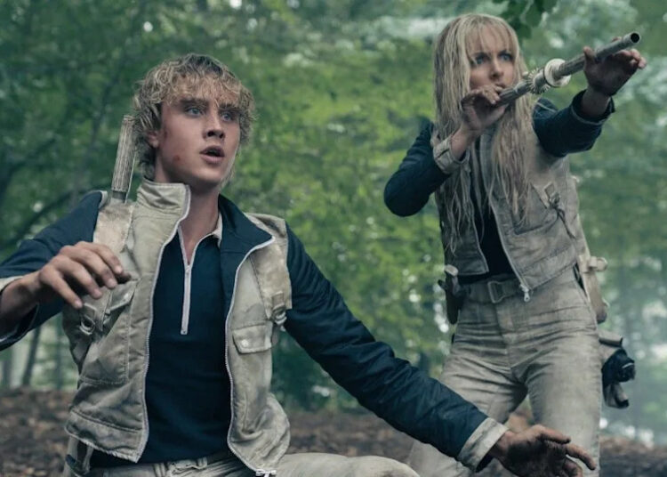 From left to right: Joseph Zada kneeling with his arms out and he looks shocked. McKenna Grace standing behind him and holding up a blowdart in Sunrise on the Reaping. .
