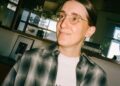 Woman with tied back hair and glasses in a plaid shirt.