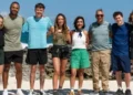 BBC The eight celebrity contestants standing in a row with their arms around each other in front or rocks and the sea