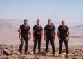 DS Rudy, DS Chris, DS Foxy and DS Billy wearing a black t-shirt and trousers, looking ahead on top of a mountain.