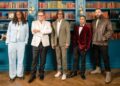 The final five contestants of The Celebrity Traitors stand in a line in front of a large book case looking at the camera with serious expressions.