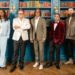 The final five contestants of The Celebrity Traitors stand in a line in front of a large book case looking at the camera with serious expressions.